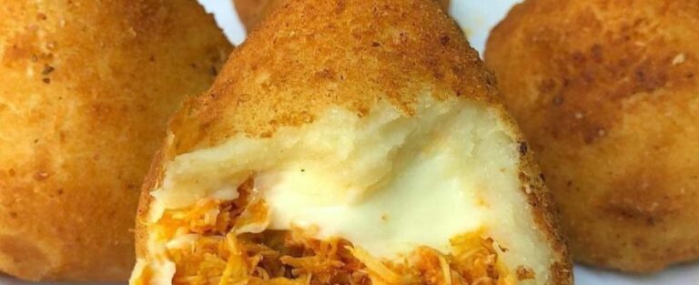 A close-up view of several Coxinha arranged on a plate. The golden croquettes have a teardrop shape and are dusted with a light layer of flaky sea salt. Keywords: