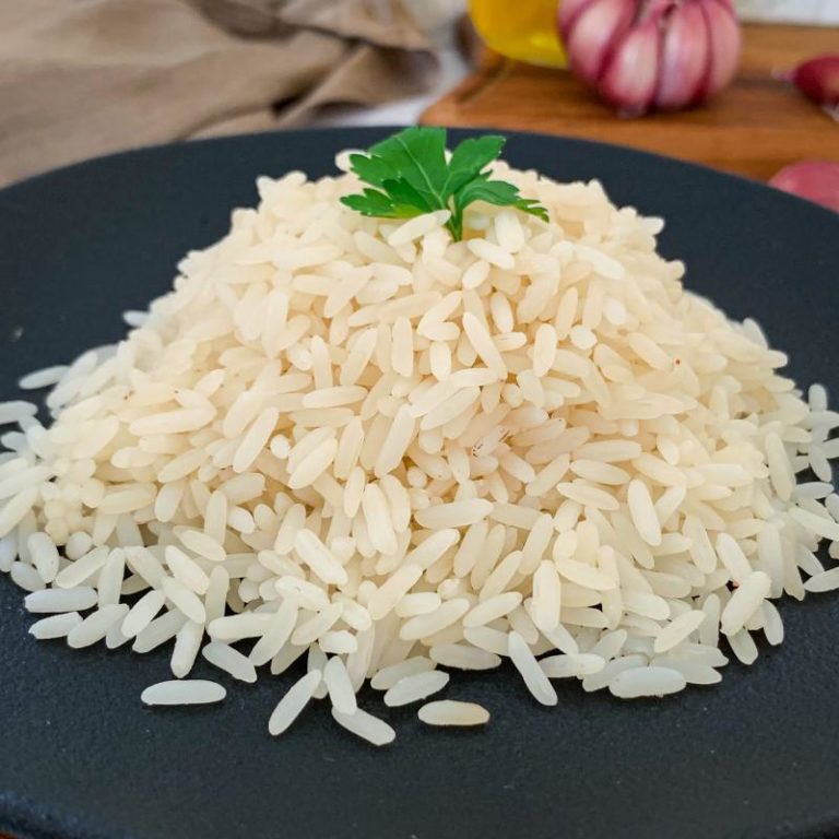 A close-up view of a fluffy white rice pilaf in a bowl, garnished with a sprig of fresh parsley.