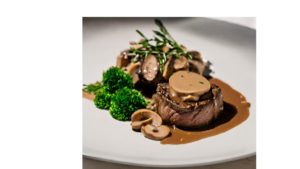 A picture of a Filé ao Molho Madeira dish. The dish consists of filet mignon medallions that are topped with a Madeira wine sauce and mushrooms. The medallions are surrounded by parsley.