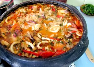 A rustic clay pot overflowing with fish, shrimp, and lobster in a vibrant red broth, garnished with fresh cilantro this is a authentic Brazilian Seafood.