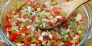 A bowl of Molho Vinagrete, with a tomato, onion, and pepper garnish.