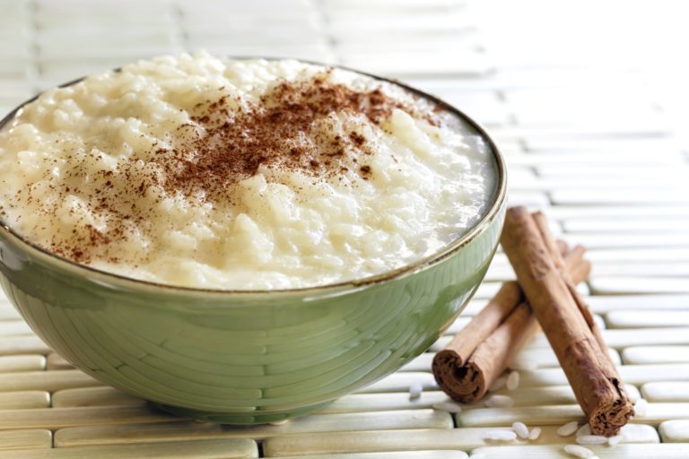 A close-up view of a bowl filled with creamy rice sprinkled with cinnamon, with a cinnamon stick resting on the side.