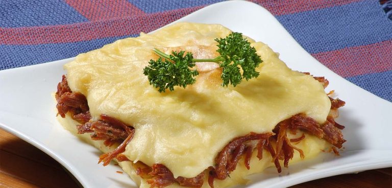 A close-up view of a steaming casserole dish filled with Creamy Mashed Cassava with Savory Shredded Beef, with a sprinkle of fresh parsley.