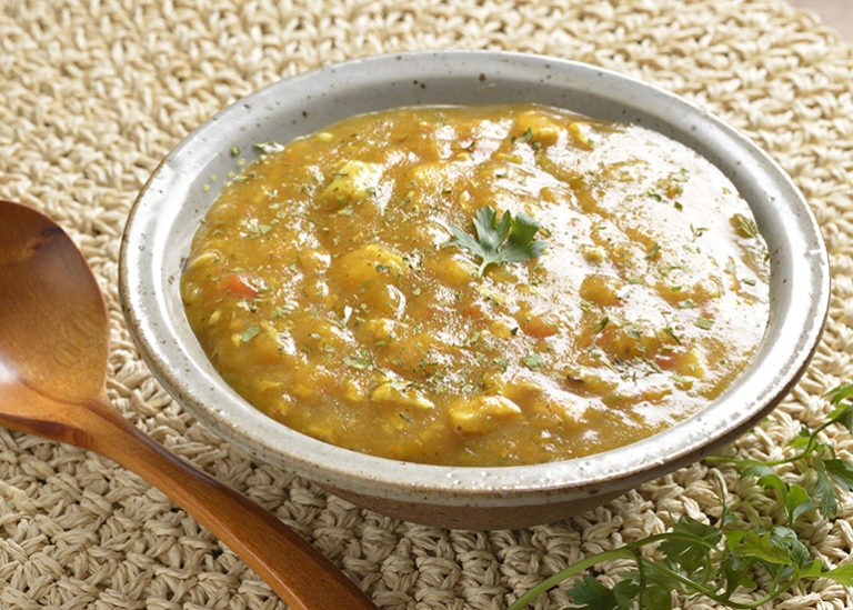 A rustic bowl overflowing with a thick, golden fish stew garnished with fresh chopped herbs.