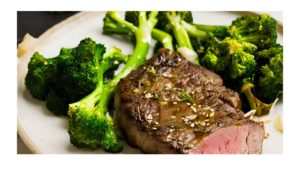 A picture of a grilled alcatra steak with garlic and broccoli. The steak is sliced and topped with the grilled broccoli.