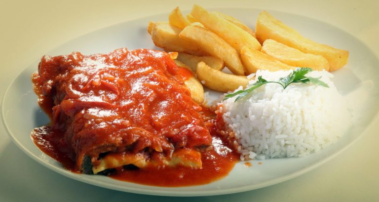 A picture of a Parmegiana do Alemão dish. The dish consists of a thick cut of filet mignon that is breaded and fried and then topped with tomato sauce and cheese. The cheese is melted and bubbly. The dish is served with rice and potatoes.