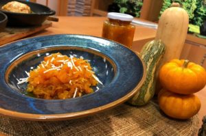 A close-up view of a glass bowl filled with Pumpking Compote, garnished with a cinnamon stick and a sprinkle of pumpkin seeds.