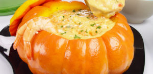 A halved pumpkin overflowing with plump shrimp bathed in a creamy tomato sauce, garnished with fresh herbs.